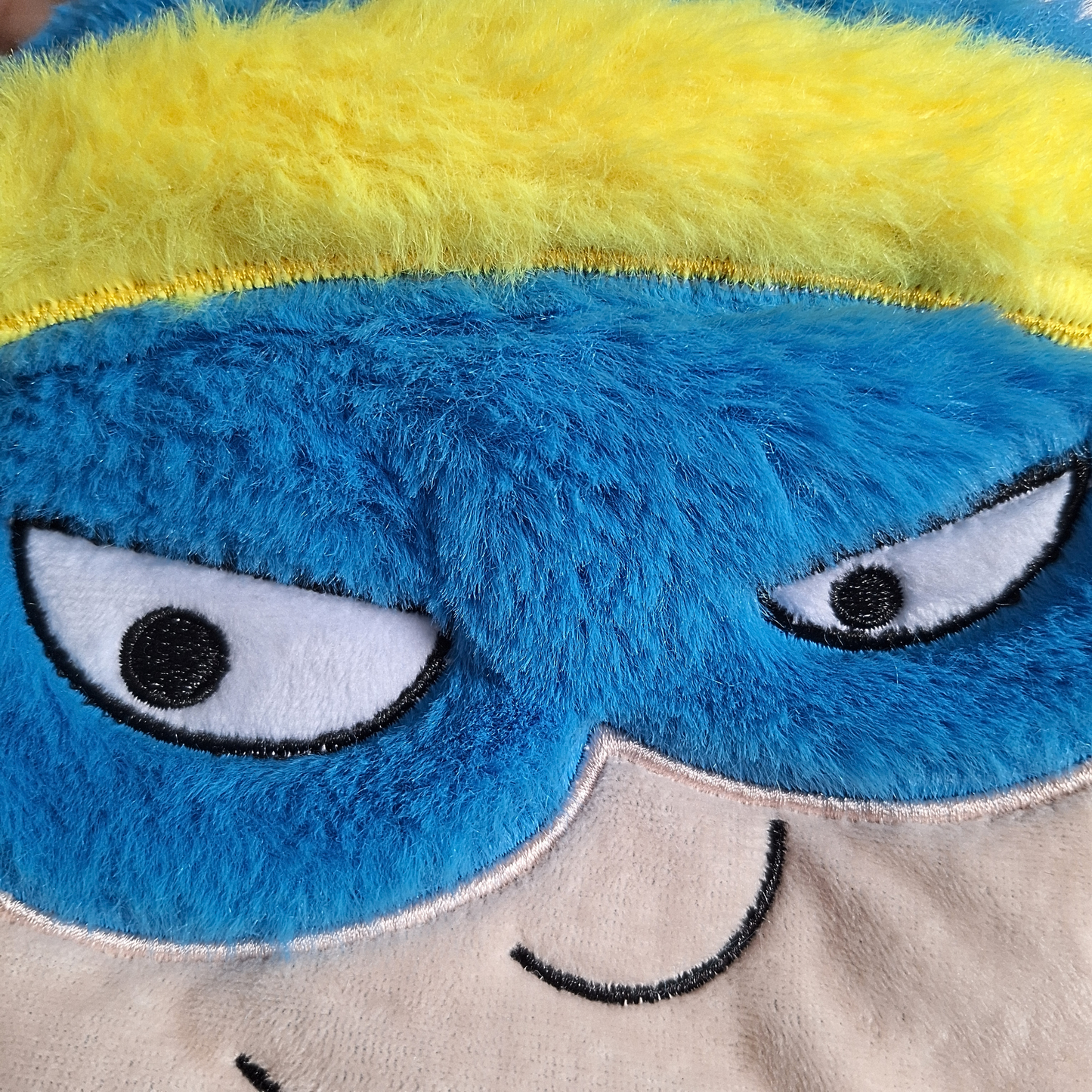 Close-up of a plush toy with blue face, yellow hair, and gray body.